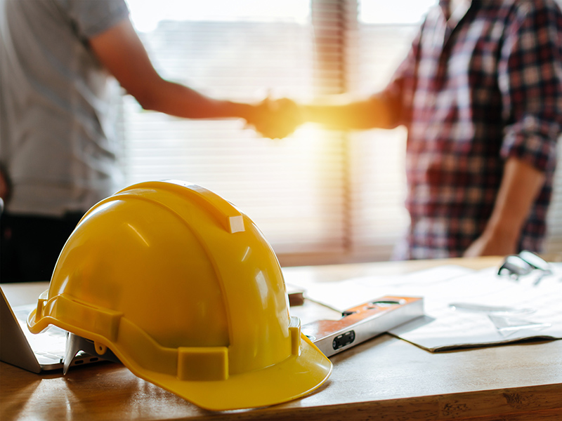 Yellow,Safety,Helmet,On,Workplace,Desk,With,Construction,Worker,Team